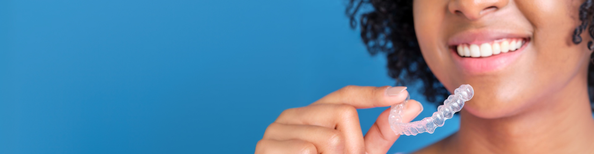 Woman holding clear aligner in front of her smile.